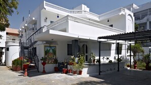 Un edificio blanco con un balcón, plantas en macetas y una escalera que lleva a la entrada.