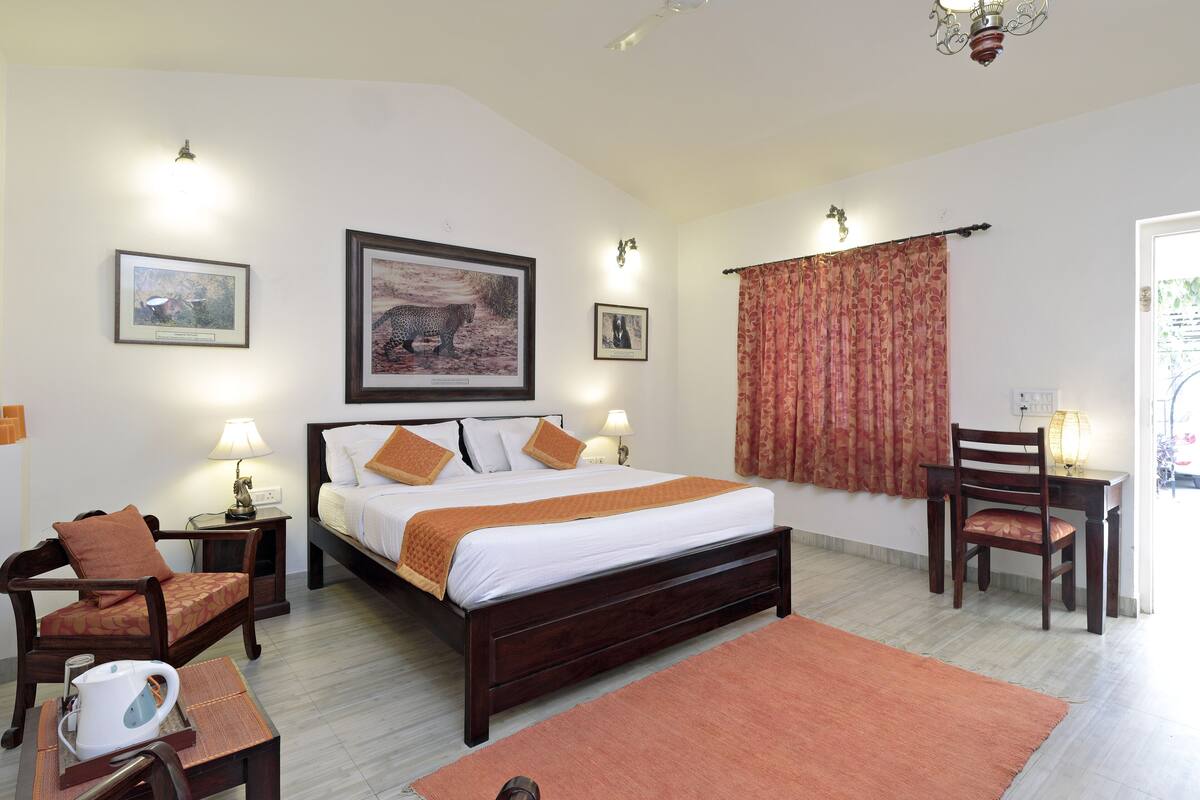 A bedroom with a large bed, two bedside tables with lamps, a wooden chair, a desk with a chair, and a large window with curtains.