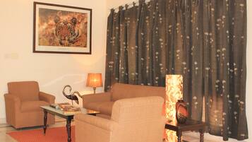 A living room with a sofa, a coffee table, a lamp, a framed tiger picture, and a curtain with a floral pattern.
