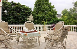 Una terraza con muebles de mimbre y una mesa lista para dos personas, rodeada de exuberante follaje.