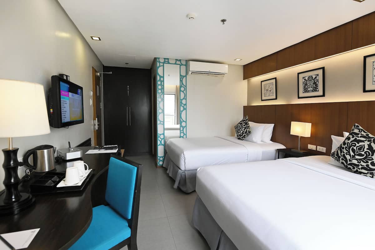 A hotel room with two beds, a desk with a computer, a coffee maker, and a TV.