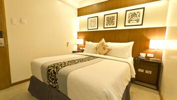 Una habitación de hotel con una cama grande, dos mesitas de noche con lámparas, un cabecero de madera y tres cuadros en la pared.