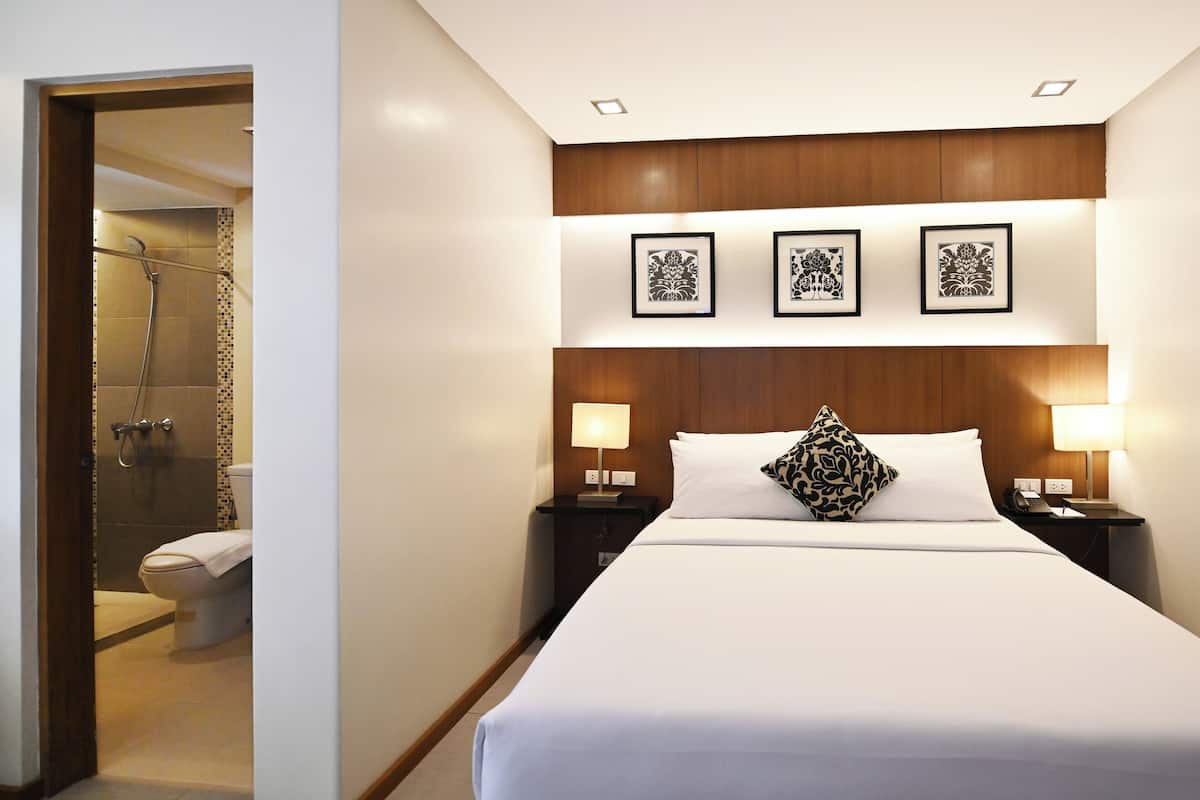 A hotel room with a large bed, two bedside lamps, a wooden headboard, and three framed pictures on the wall.