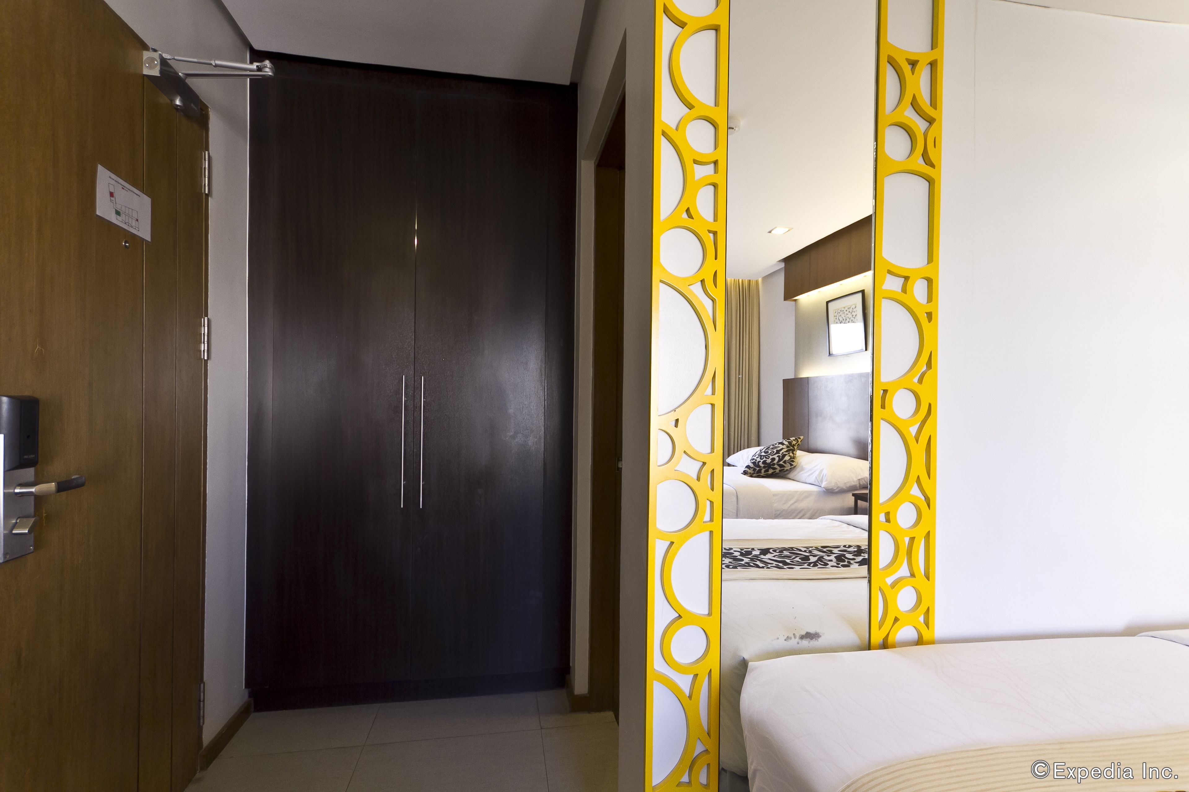A hotel room with a dark wooden door, a bed with white bedding, and a yellow decorative partition.