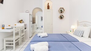Una habitación de hotel con cama, escritorio y silla. Hay una mesita con una botella y vasos.