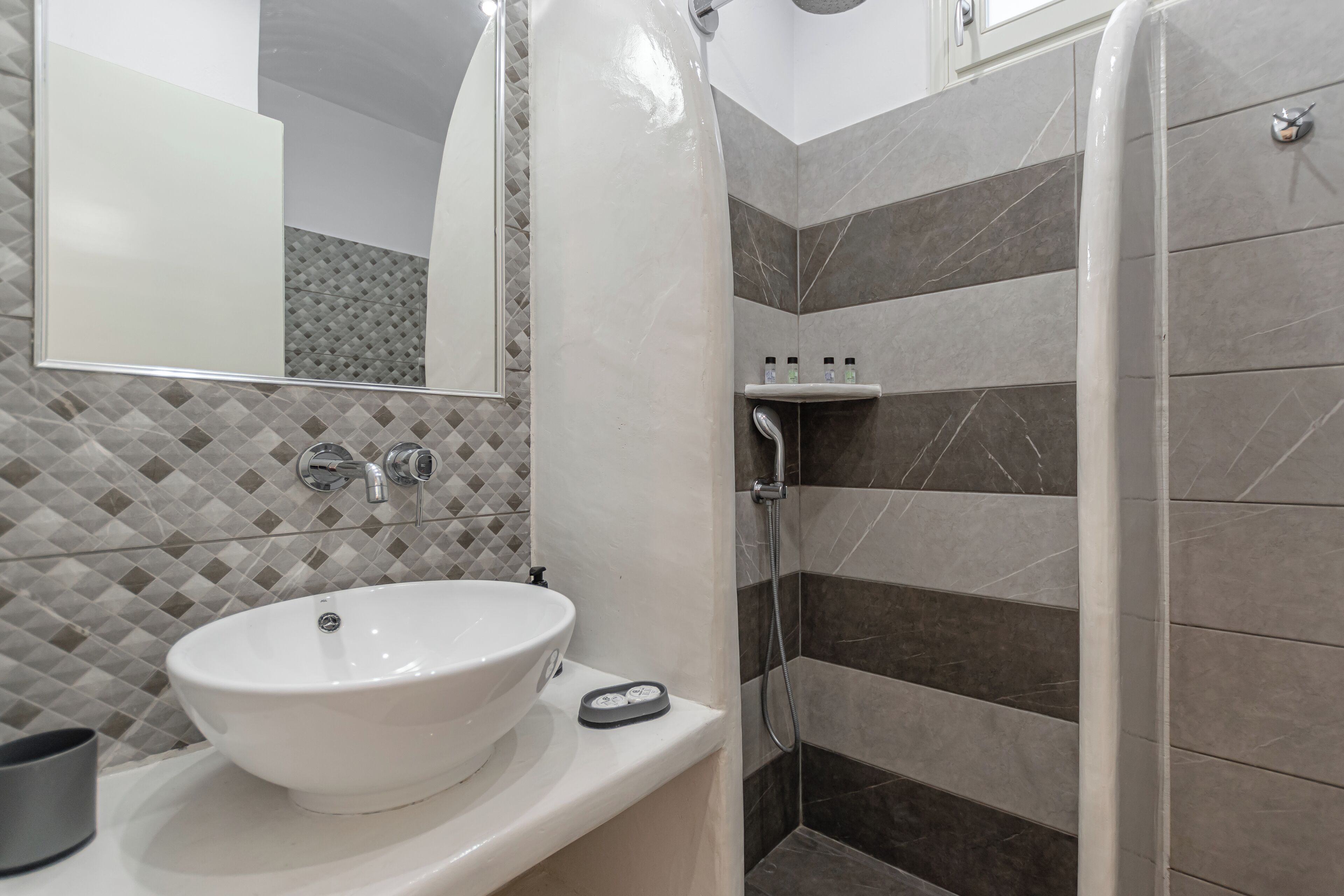 A bathroom with a white sink, a mirror, and a shower area with dark tiles.