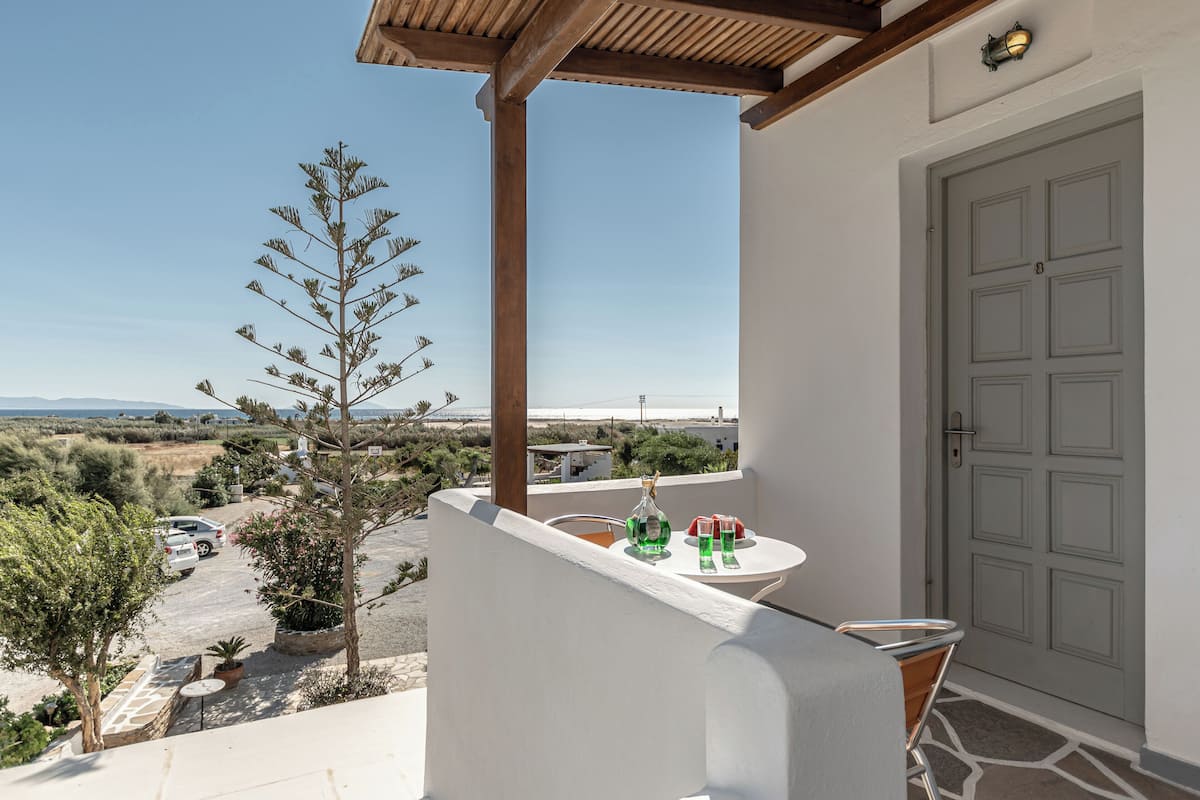 A balcony with a view of the countryside, a table with drinks, and a door.