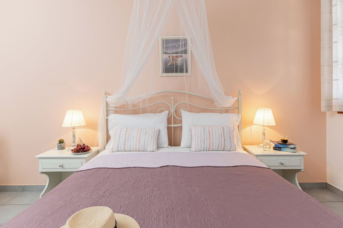 A bedroom with a four-poster bed, two bedside tables with lamps, and a nightstand with a book and a glass.