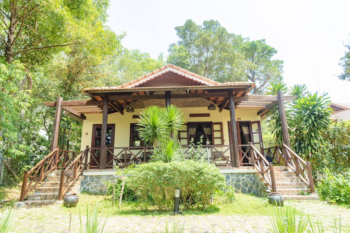 Una casa de dos pisos con techo de tejas, escalera de madera y base de piedra.