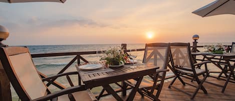 A wooden deck with tables and chairs overlooking the ocean at sunset.