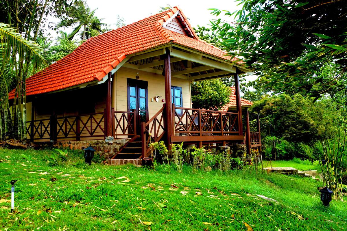Una casa con techo de tejas rojas, porche de madera y un jardín con césped y plantas.
