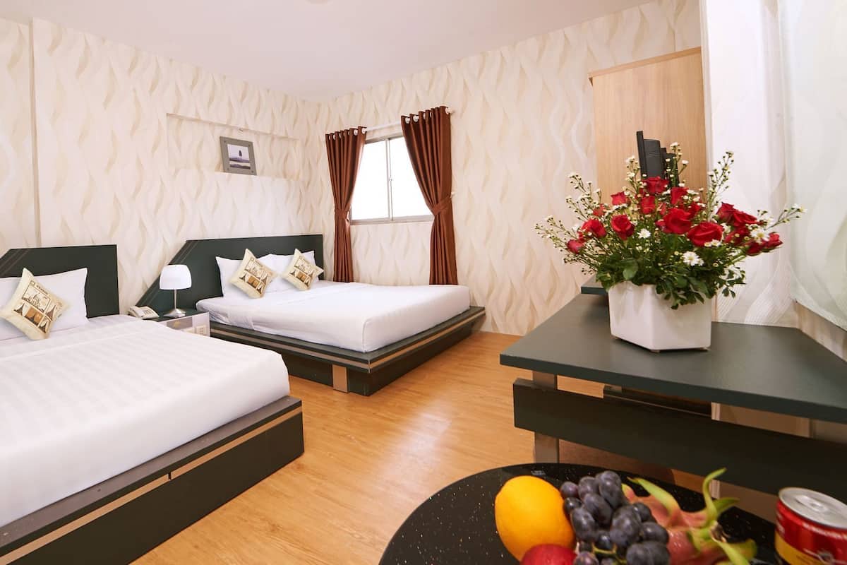 A hotel room with two beds, a desk, a vase of flowers, and a fruit bowl.