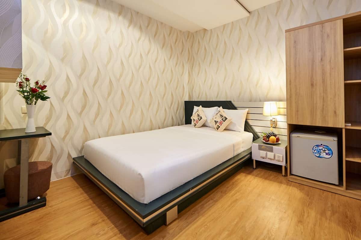 A bedroom with a bed, bedside table, lamp, and a small refrigerator.