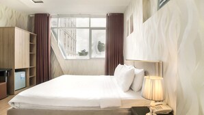 A hotel room with a bed, a nightstand with a lamp and phone, a wardrobe, and a window with curtains. - Saigon Charm Hotel (Ho Chi Minh City)