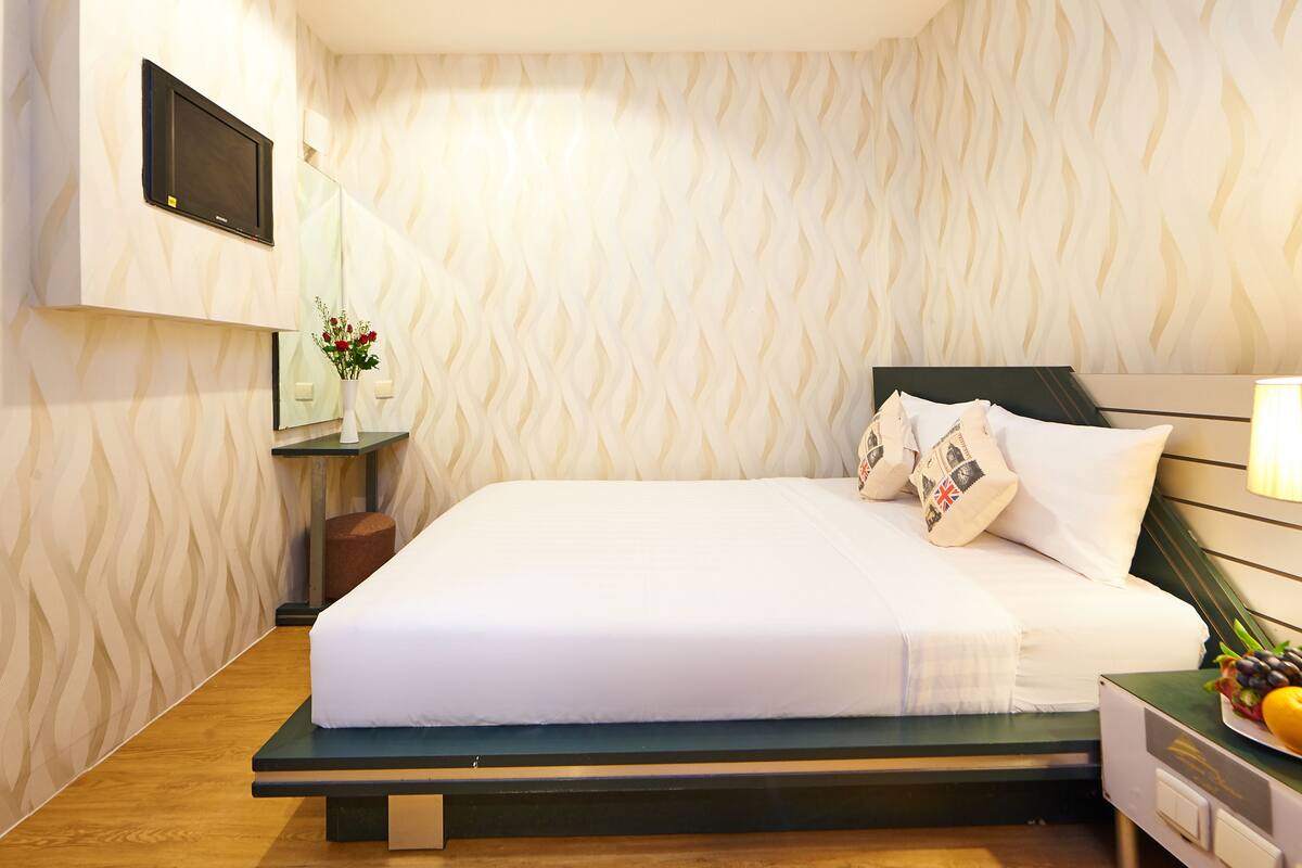 A neatly made bed with white linens, a bedside table with a lamp, and a wall-mounted TV.