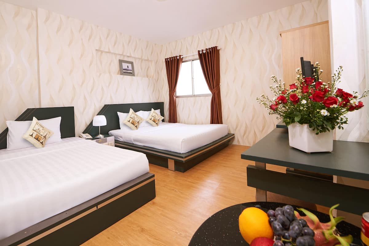 A hotel room with two beds, a desk, a vase of flowers, and a fruit bowl.