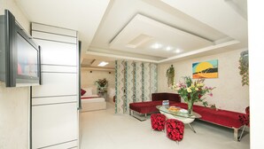 A modern living room with a flat-screen TV, red and black patterned sofas, a glass coffee table, and a painting on the wall. - Saigon Charm Hotel (Ho Chi Minh City)
