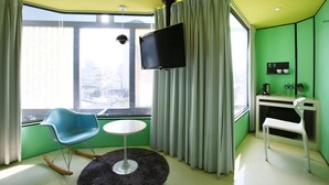 A modern room with a large window, a flat-screen TV, a small round table, and a desk with a chair. - The Icon Hotel (Kaohsiung)