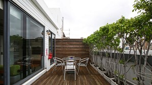 A wooden deck with a table and chairs, a glass door, and potted plants. - The Icon Hotel (Kaohsiung)