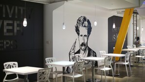 A modern dining area with white tables and chairs, a large black and white mural, and hanging light bulbs. - The Icon Hotel (Kaohsiung)