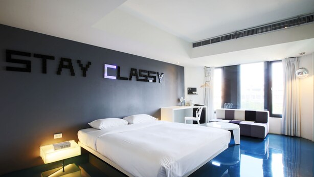 A modern hotel room with a large bed, a sofa, a desk, and a wall with the words "STAY CLASSY". - The Icon Hotel (Kaohsiung)