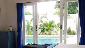 A hotel room with a bed, a small desk, and a view of a swimming pool. - Villa Sari Agung (Tibubeneng)