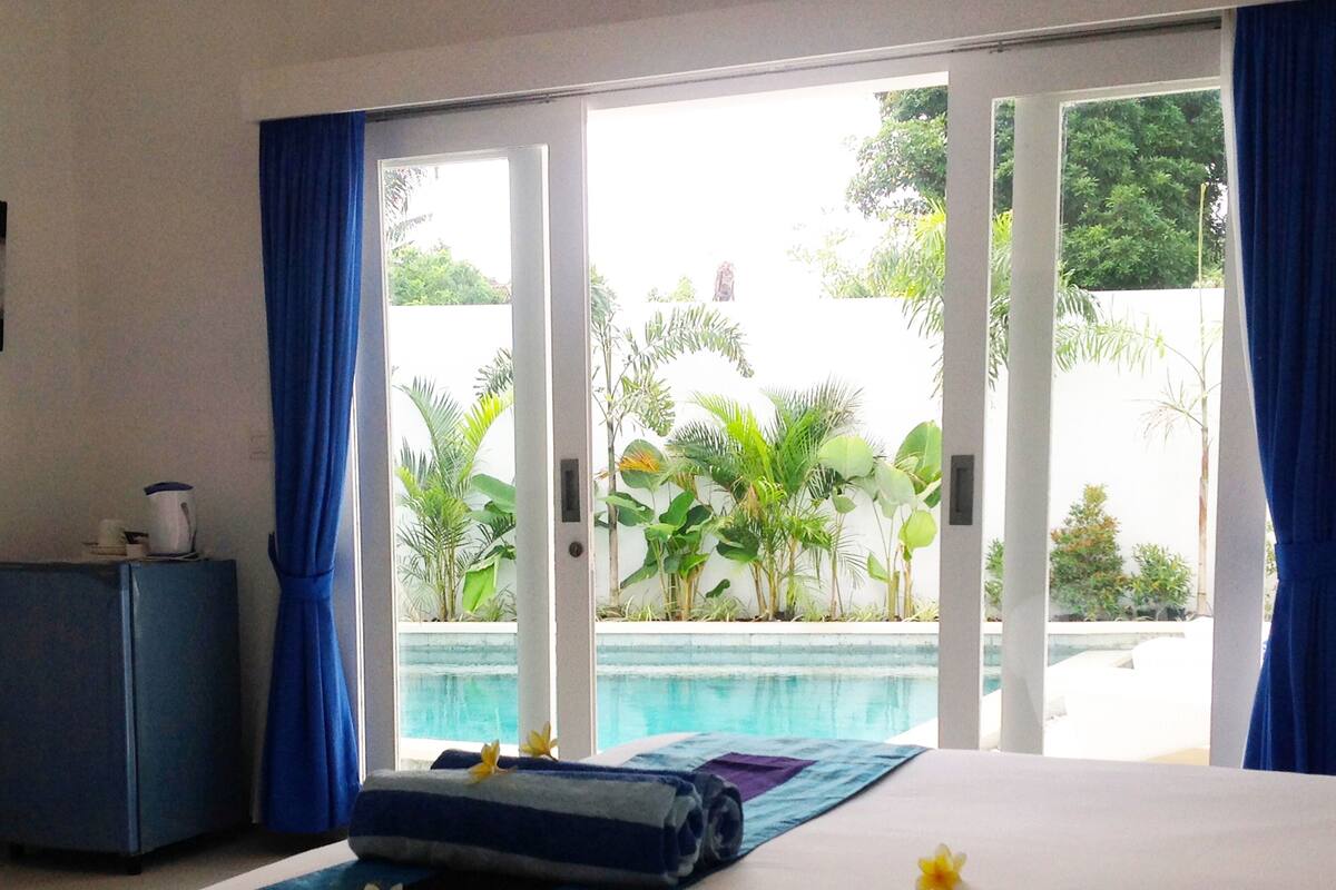 A hotel room with a bed, a small desk, and a view of a swimming pool.