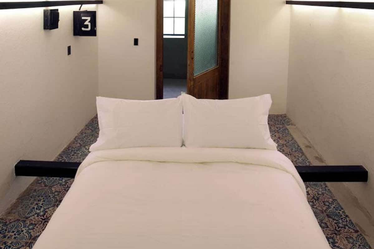 A minimalist hotel room with a bed, a door with frosted glass, and a number '3' sign on the wall.
