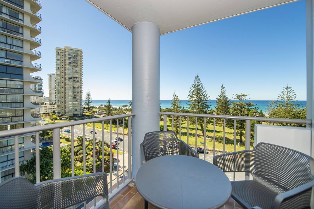A balcony with a table and chairs, overlooking a cityscape and a body of water.