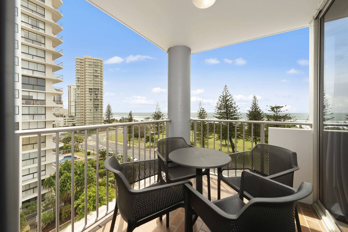 A balcony with a round table and four chairs, overlooking a cityscape and the ocean.