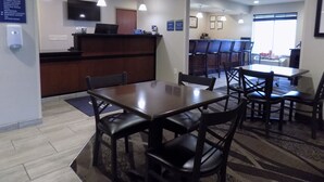 Un vestíbulo de hotel con una recepción, un comedor con mesas y sillas, y una zona de bar con taburetes.