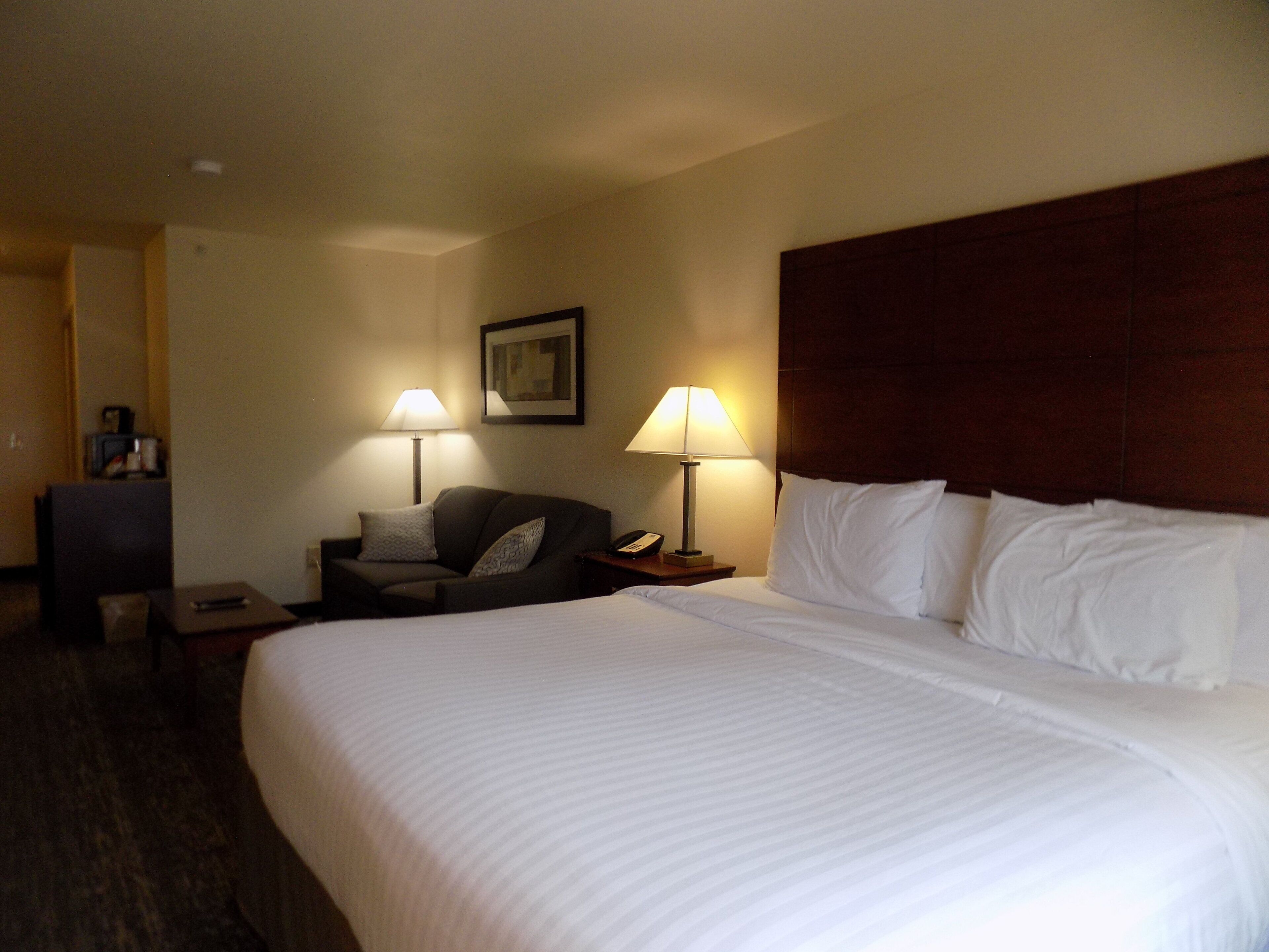 Una habitación de hotel con una cama grande, dos mesitas de noche, un escritorio, una silla y dos lámparas.