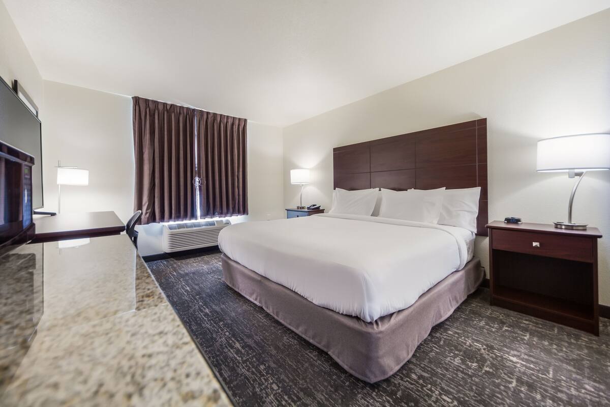 Une chambre d’hôtel avec un grand lit, un téléviseur à écran plat, un bureau avec une lampe et une fenêtre avec des rideaux.