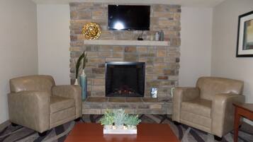 A living room with a stone fireplace, two leather armchairs, a wooden coffee table, and a flat-screen TV mounted above the fireplace.