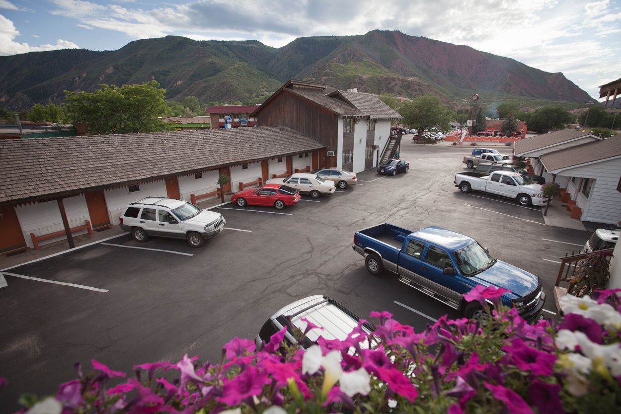 A parking lot with several cars, a building with a sloped roof, and mountains in the background.