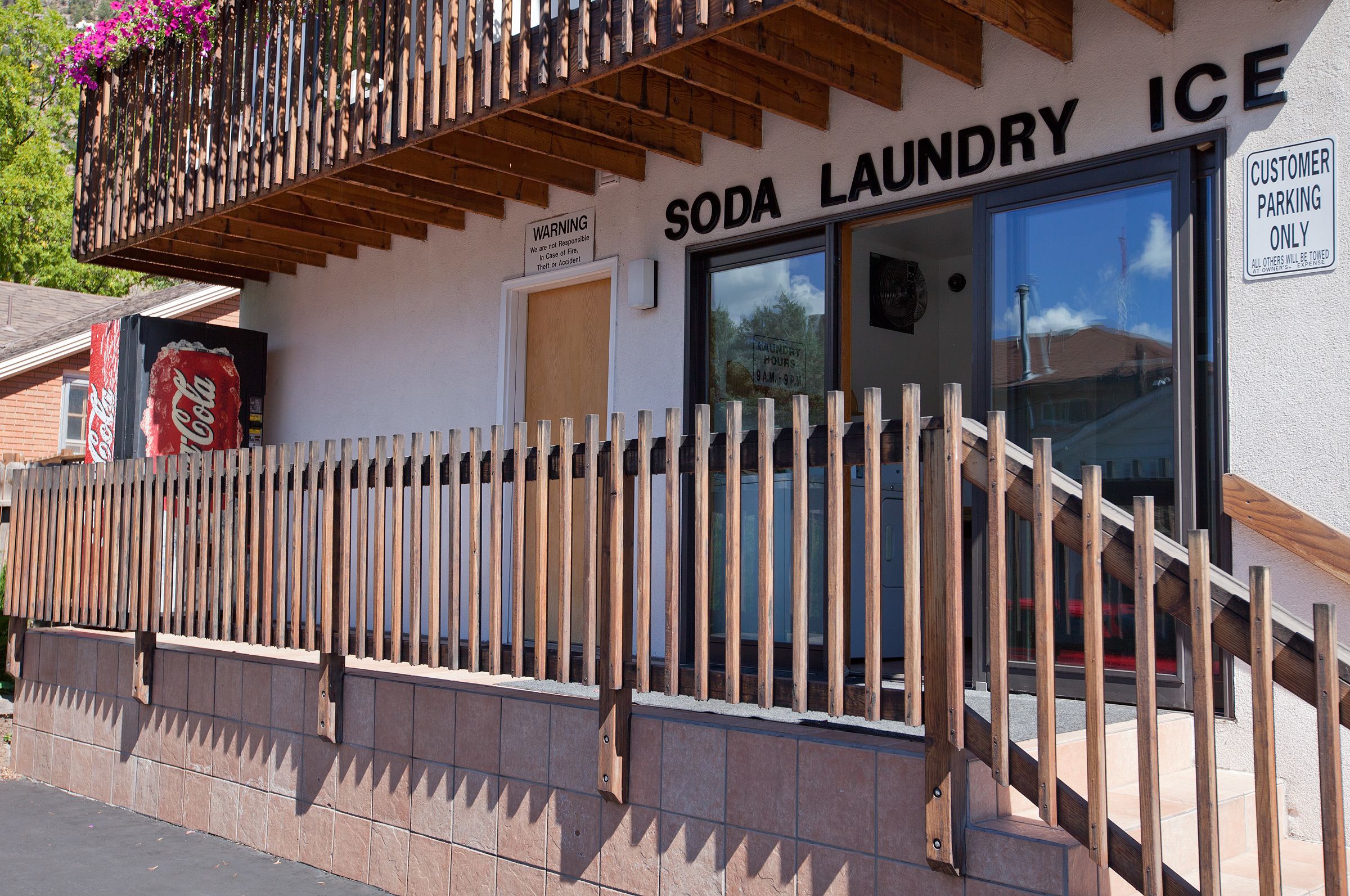 Eine Schaufensterfront mit Holzzaun, einem Coca-Cola-Schild und einem Schild mit der Aufschrift 'SODA LAUNDRY ICE' sowie Kundenzufahrtsmöglichkeiten.