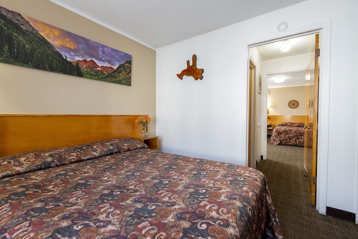 A hotel room with a large bed, a painting of a mountain landscape, and a wooden headboard.