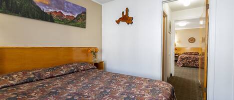 A hotel room with a large bed, a painting of a mountain landscape, and a wooden headboard.
