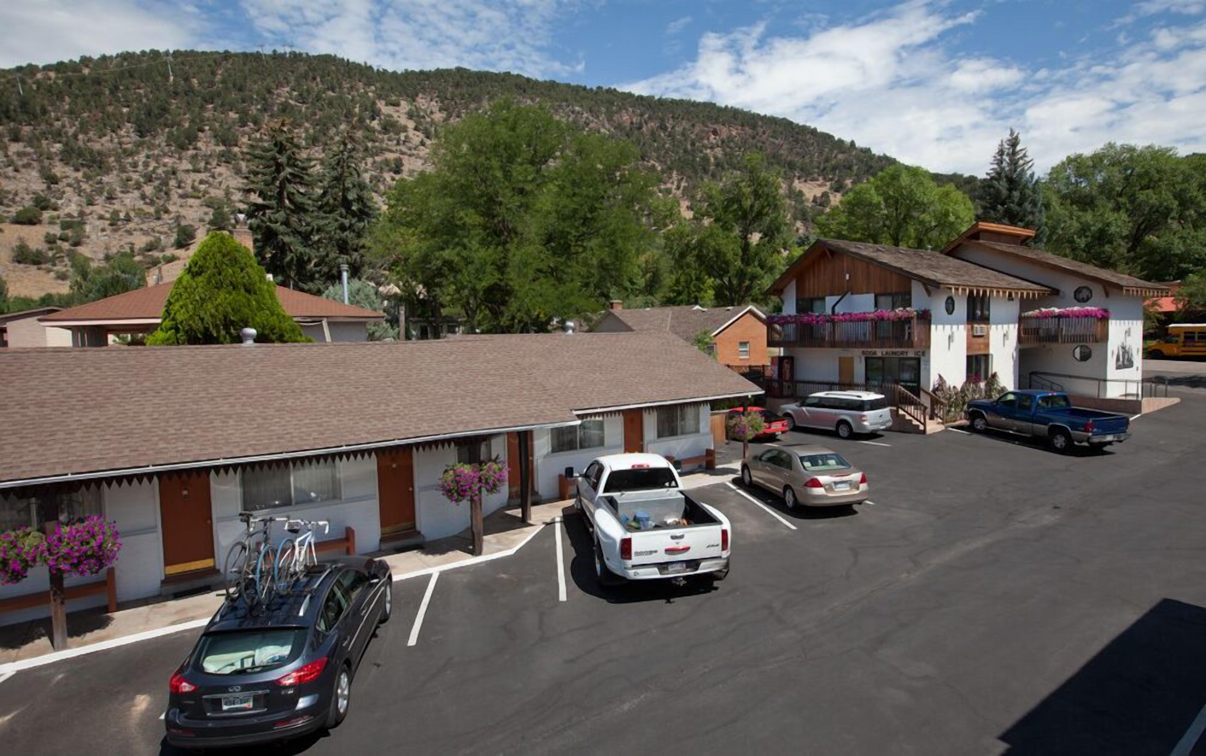 Un estacionamiento con varios coches, un edificio con un letrero que dice 'SODA LAUNDRY ICE' y un paisaje montañoso de fondo.