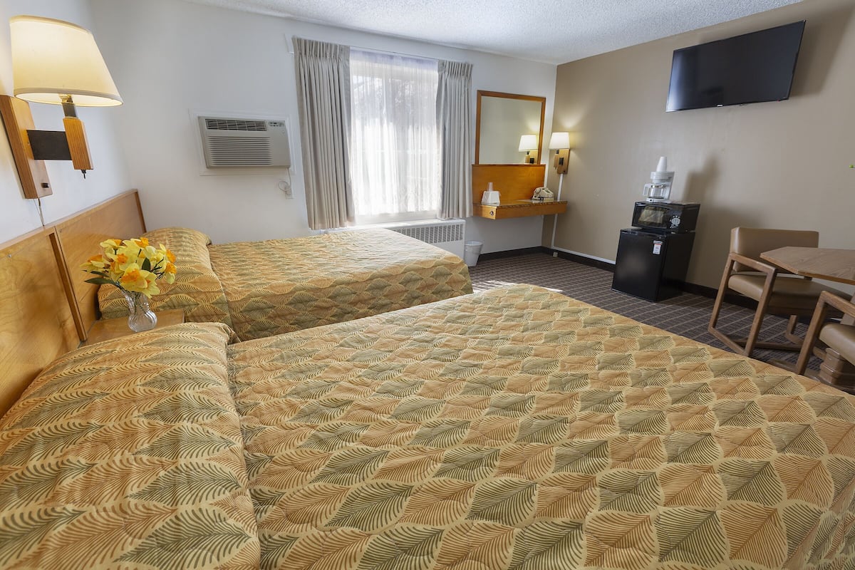 A hotel room with two beds, a desk, a chair, a TV, a mirror, and a window with curtains.