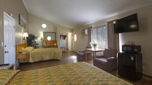 Quarto de hotel com duas camas, televisão, secretária com cadeira, frigorífico e janela com cortinas.