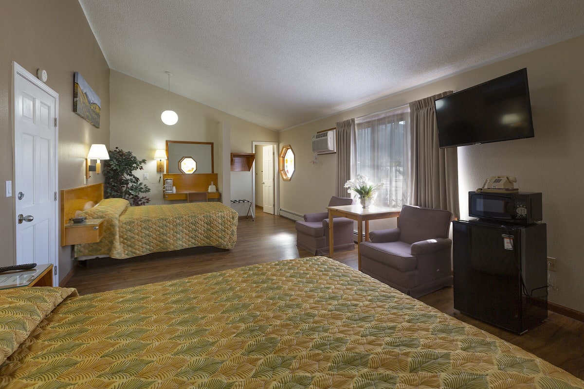 A hotel room with two beds, a television, a desk with a chair, a refrigerator, and a window with curtains.