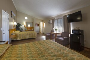 Quarto de hotel com duas camas, televisão, secretária com cadeira, frigorífico e janela com cortinas.