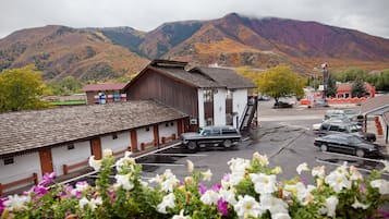 Un edificio rústico de madera con fachada blanca, un estacionamiento con varios autos, y montañas al fondo.