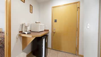 A hotel room with two beds, a small kitchenette, a wooden door, and a painting on the wall.