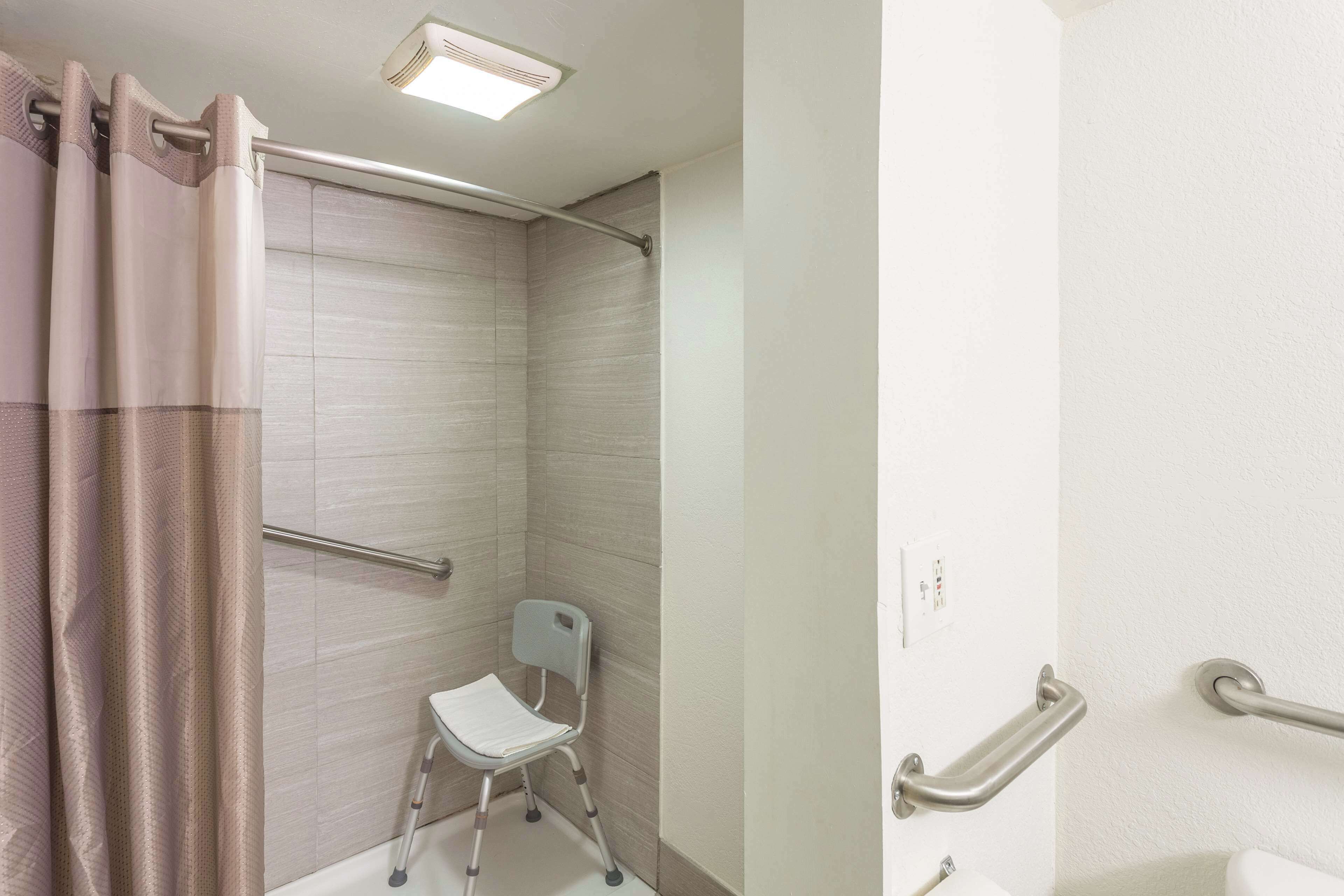 A bathroom with a shower, a white toilet, and a wheelchair-accessible chair.