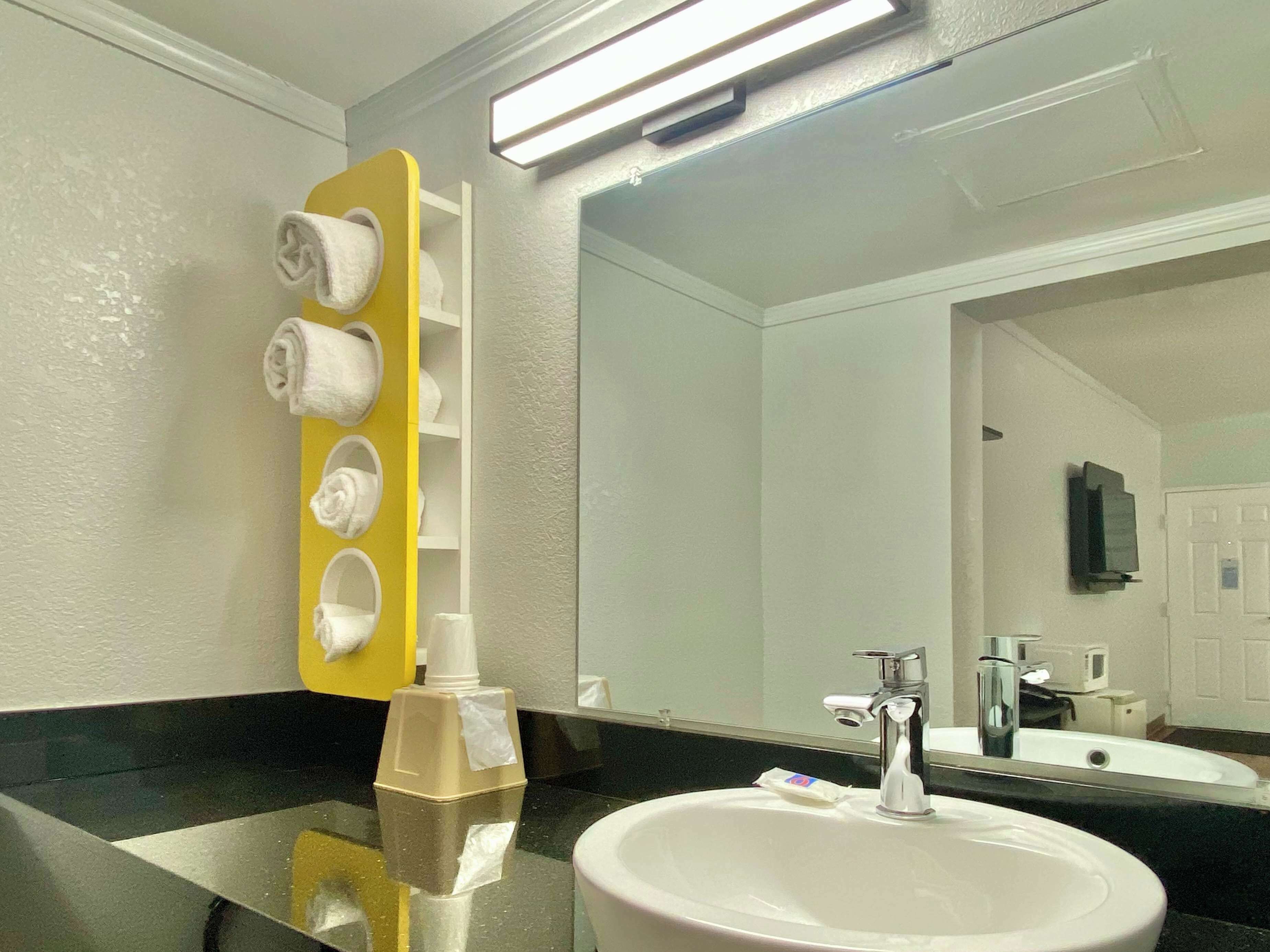 Une salle de bain avec un lavabo blanc, un miroir et un porte-serviettes jaune sur lequel sont posées des serviettes.