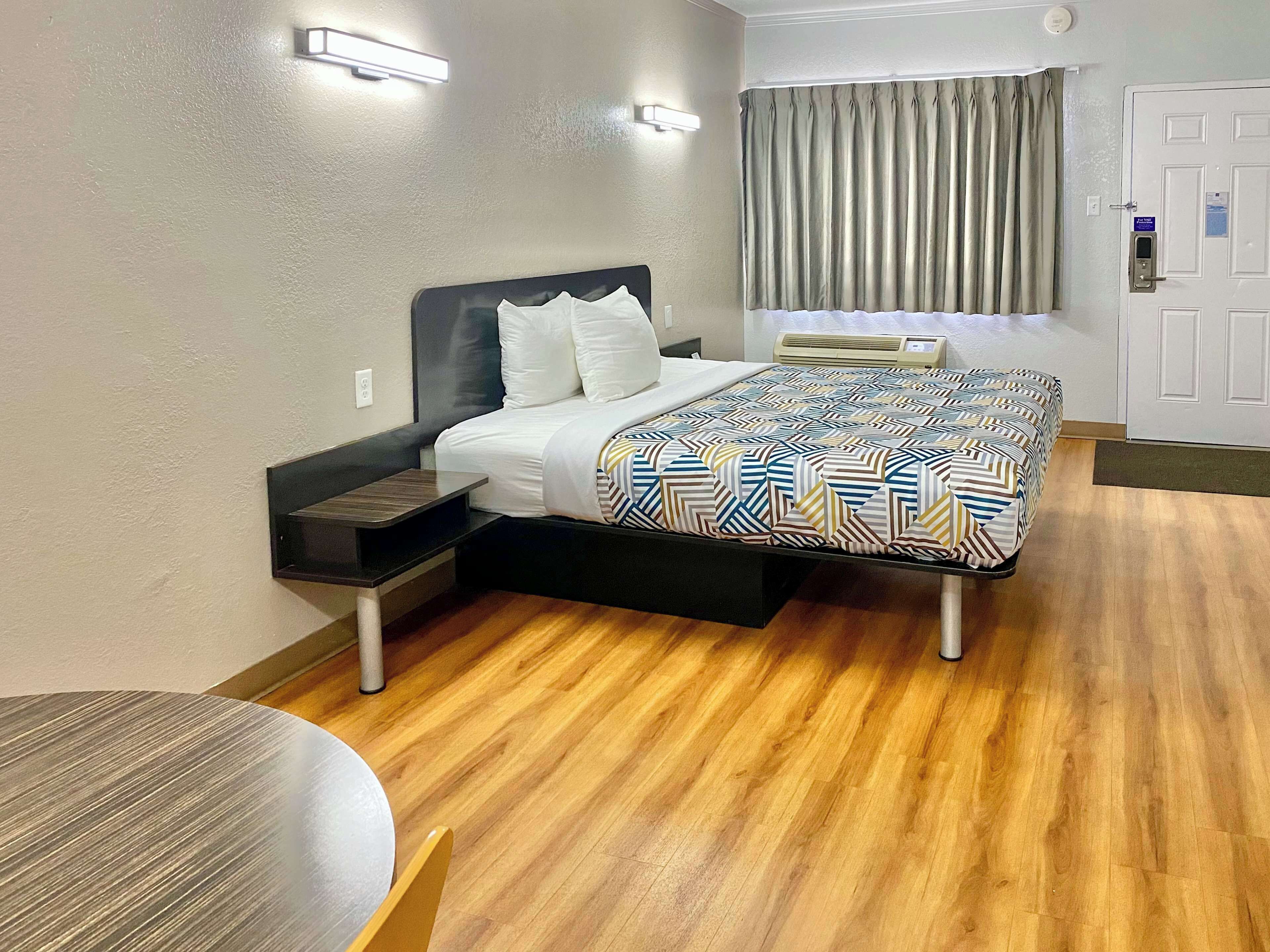 A hotel room with a bed, bedside table, and a small table with a chair.