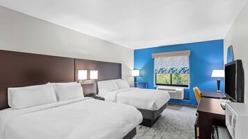 Habitación de hotel con dos camas, un escritorio, un televisor y una ventana con vistas a zonas verdes.