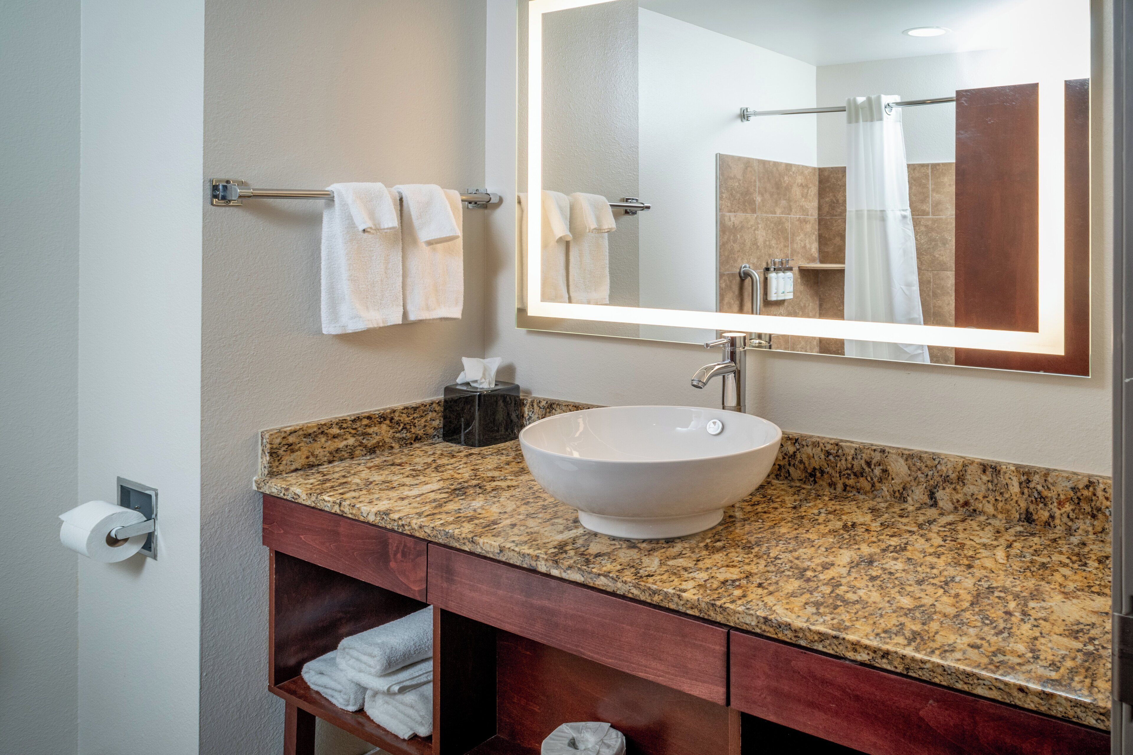 A bathroom with a granite countertop, a white vessel sink, a mirror, and a towel rack.